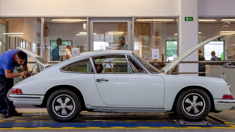 A vintage white Porsche 912 being inspected by a mechanic.