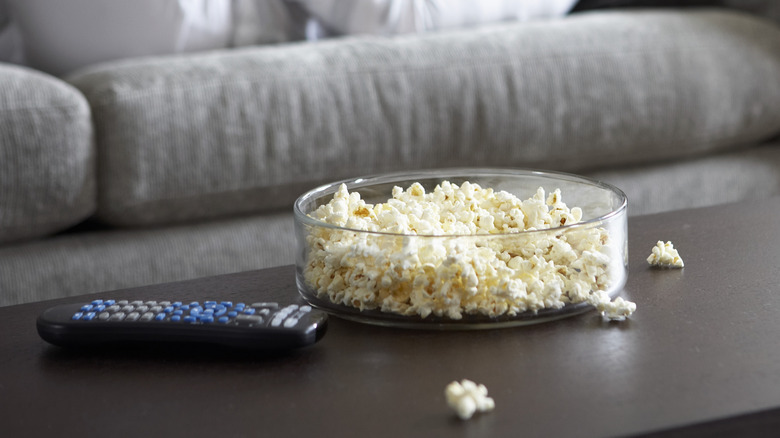 a bowl of popcorn and remote on a coffee table.