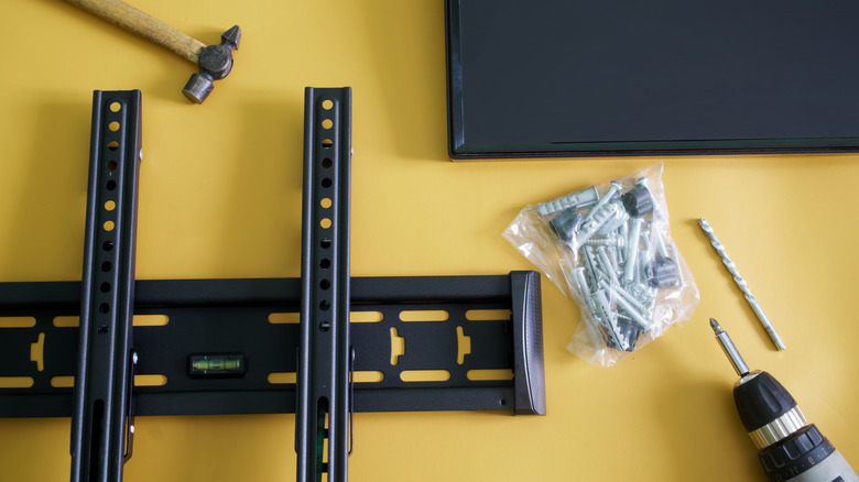 A Small TV, Wall Mount, Fasteners, And Tools Against Yellow Background