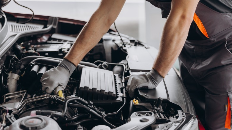 A man wearing a gray glove inspecting a car engine.