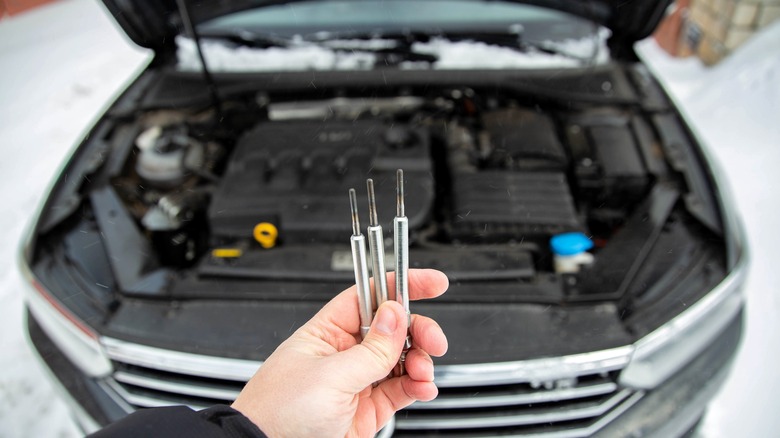 Modern ceramic glow plugs in a hand against the background of a diesel car engine