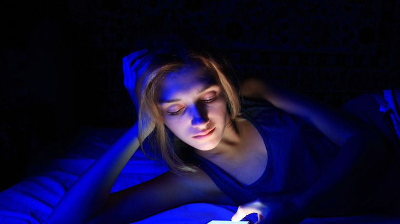 Woman lying in bed looking at her smartphone