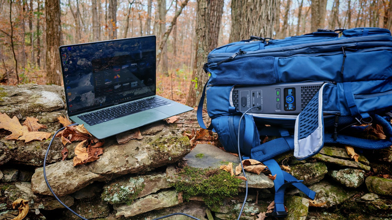 The Bluetti Handsfree 2 charging a laptop on a stone wall in the woods