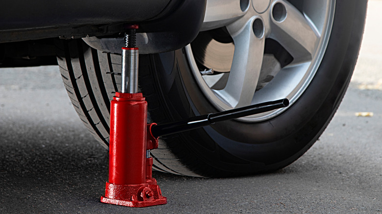 A red bottle jack positioned underneath a car on pavement.