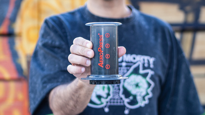 Man holds an AeroPress coffee maker with his right hand