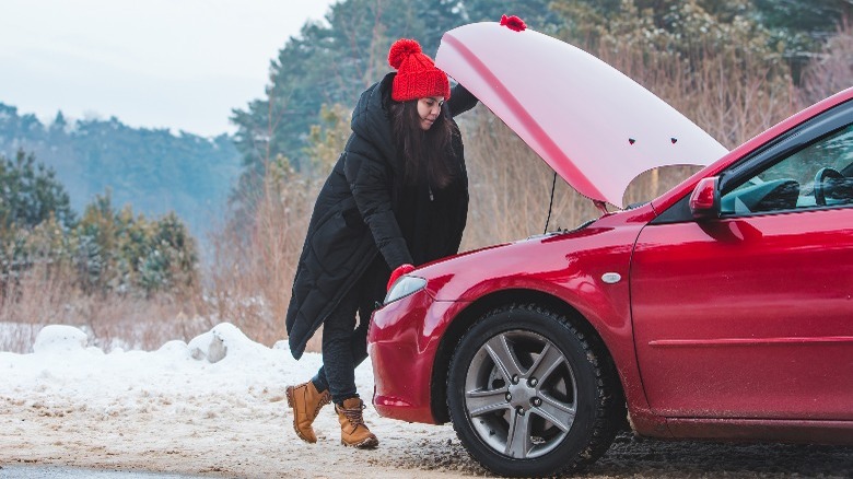 A woman troubleshoting a red car in winter