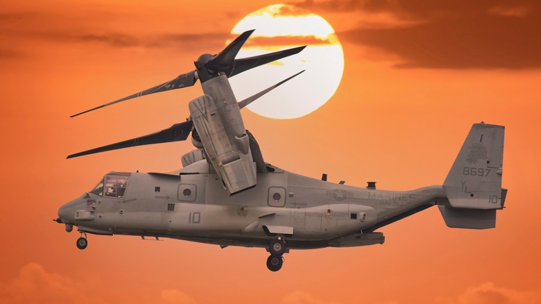 A V-22 Osprey landing vertically with the sun in the background