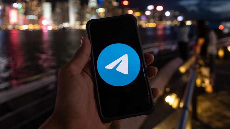 hand holding phone with Telegram logo