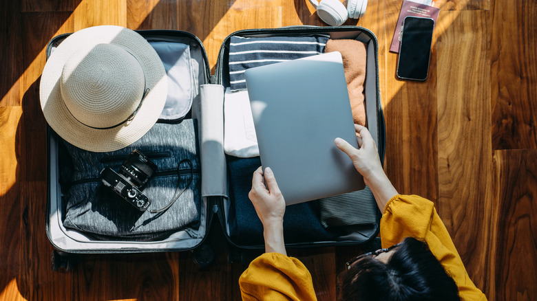 A woman is packing a laptop into her luggage