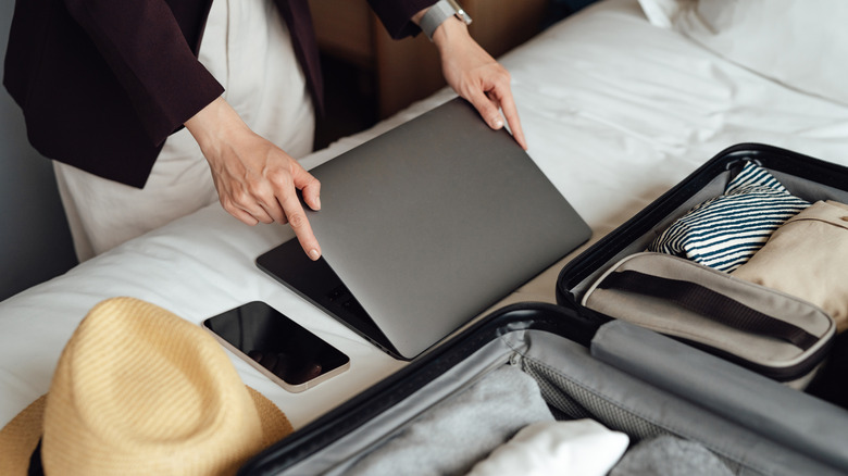 A woman is folding down a laptop that's turned off to pack it in her luggage