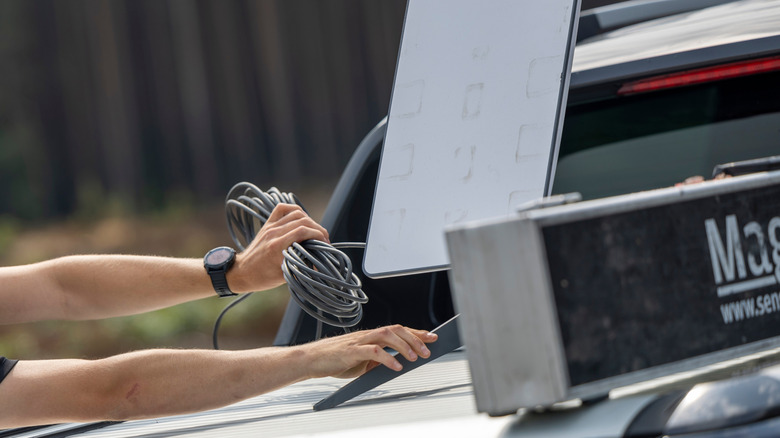 Hand holding Starlink cable and dish on top of vehicle