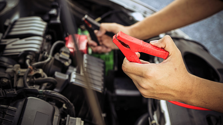 A car mechanic holds car booster cables