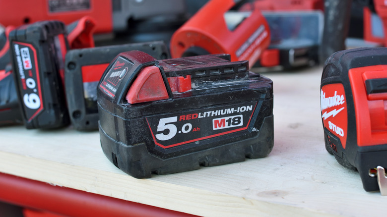 A Milwaukee battery among Milwaukee tools on a table.