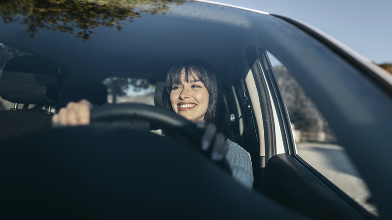 A woman smiles while driving a car with an untinted front windshield