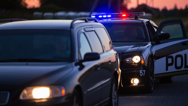 A tinted vehicle being pulled over by a police car on the side of the road