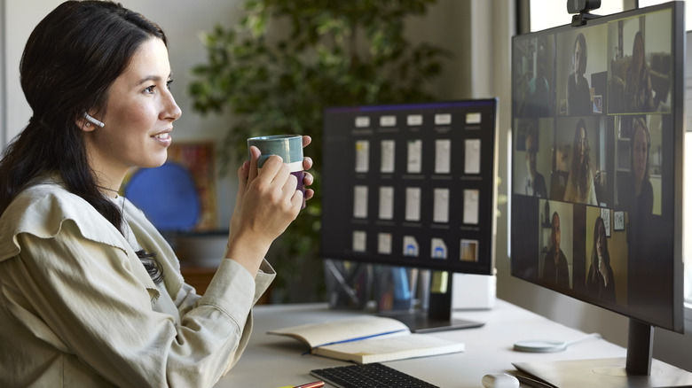 Woman holding a coffee mug and using AirPods while on a conference call on her desktop monitor