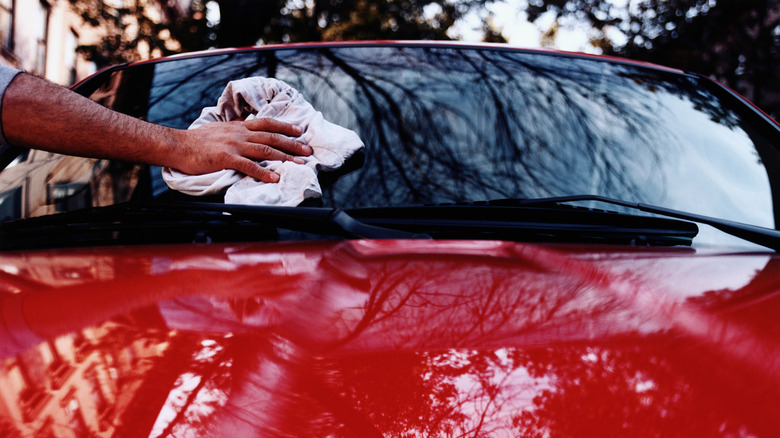 Hand holding rag and wiping car's windshield