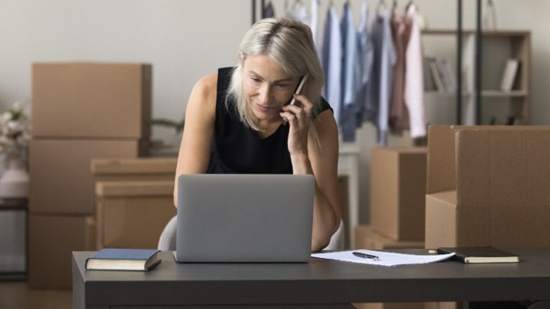 woman on phone and laptop surrounded by boxes