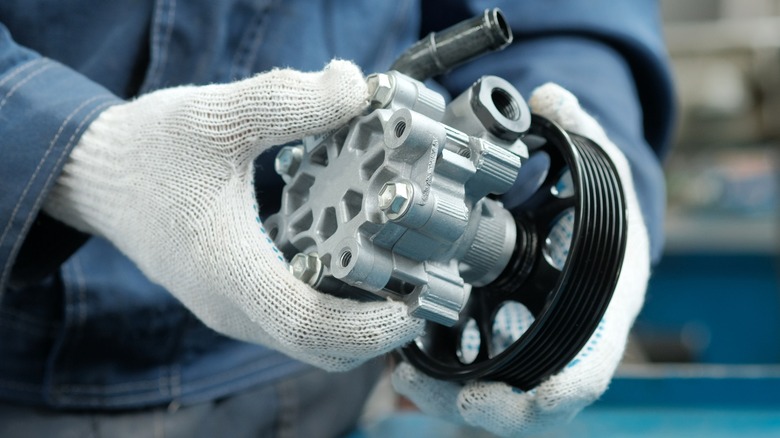 gloved hands holding a power steering pump