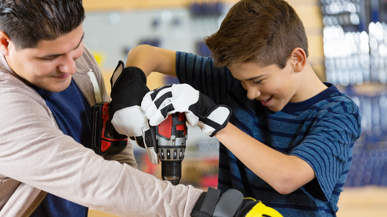 A teenager being taught how to use a power drill.