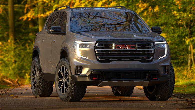 A gray GMC Acadia on a road in front of trees