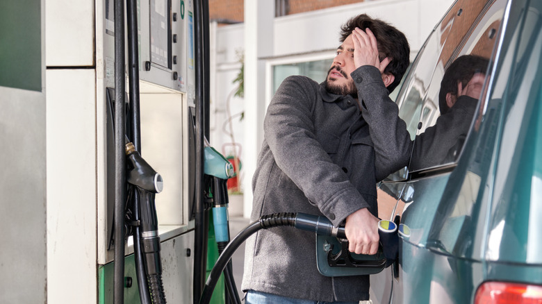 Young man refueling his vehicle while looking worried