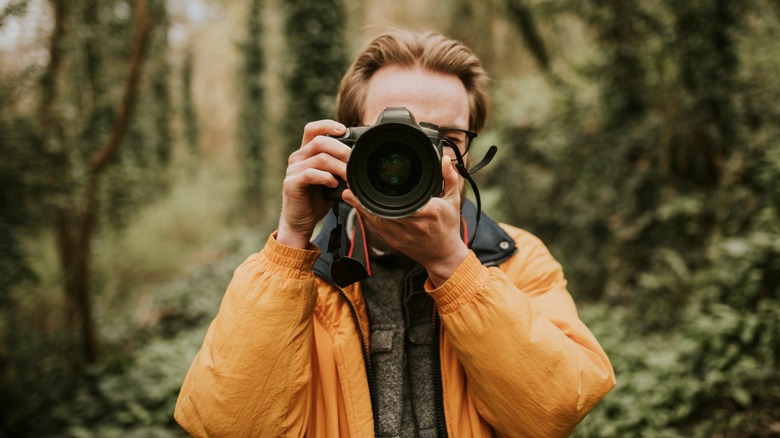 man in woods holding digital camera to eye