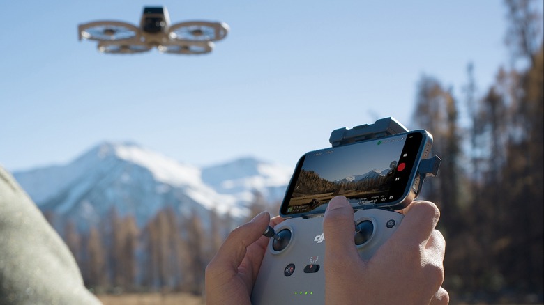 A Man Using A Remote Control And Smartphone To Fly A DJI Flip