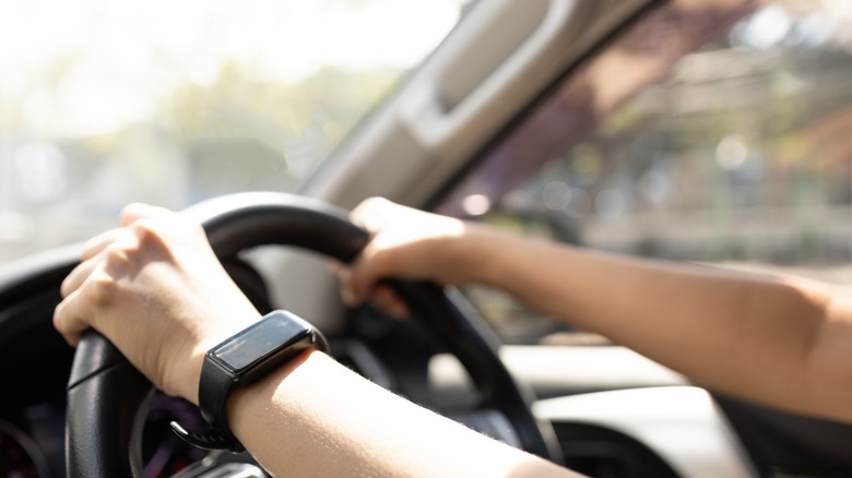 A woman's arms on a streering wheel with bright light coming through the windshield.