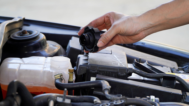 A hand checking the cap of the water level in a car engine