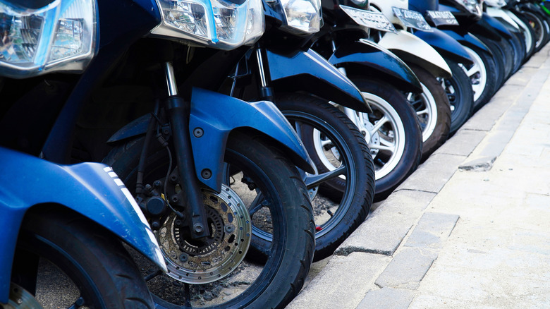 line of moped front wheels parked along a curbside