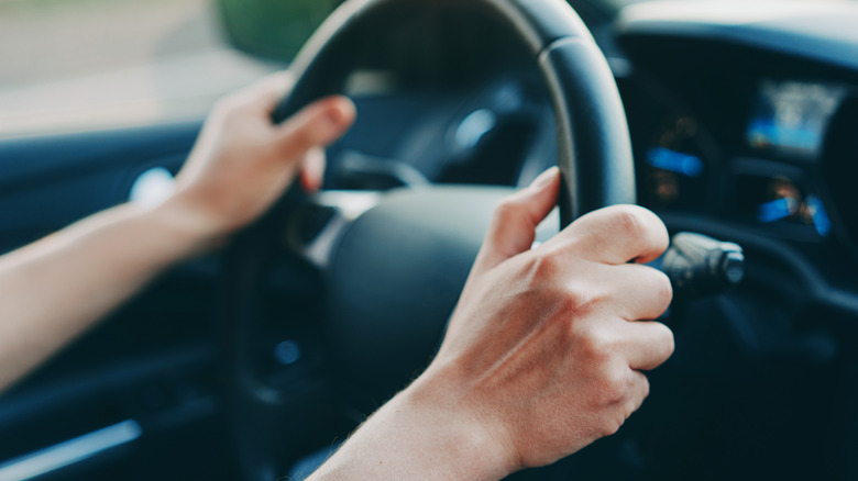 Hands holding a car steering wheel.