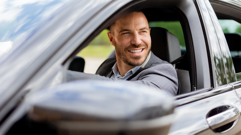 A man smiling while sitting in the driver's seat of a silver car