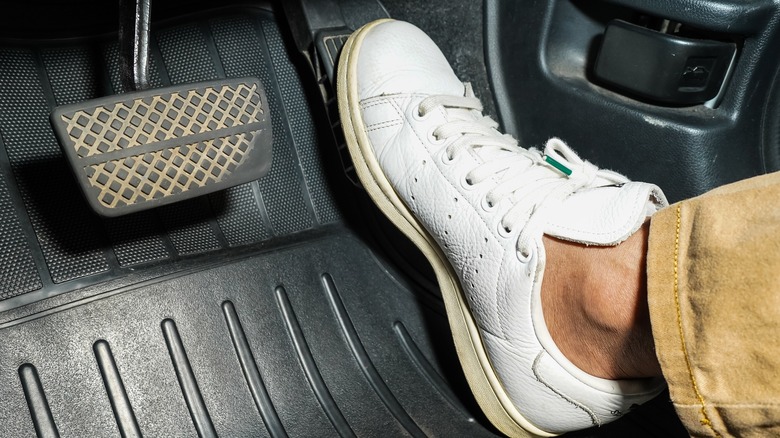 A foot clad in a white shoe stepping on a car's gas pedal.