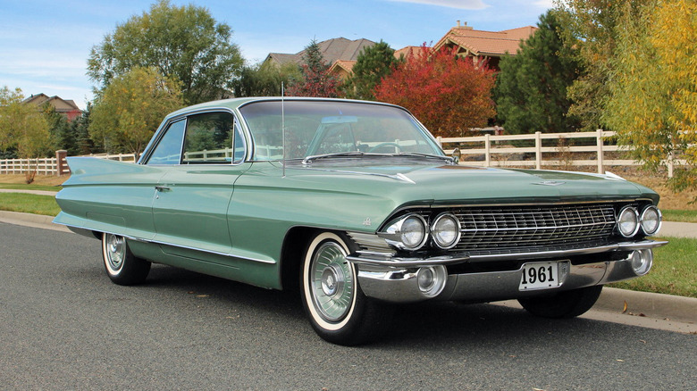 Green 1961 Cadillac Coupe de Ville parked on country road with white fence and trees in background