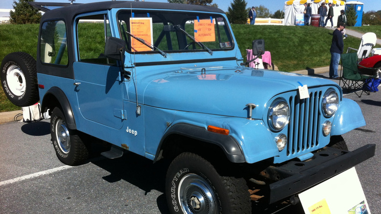 Light blue Jeep CJ7 parked in lot at car show with orange paper signs taped to windshield