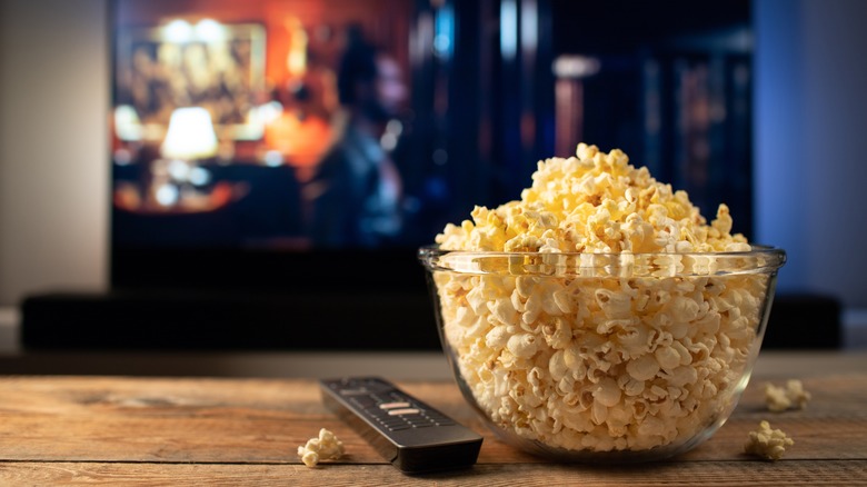 bowl of popcorn and remote control with TV in background