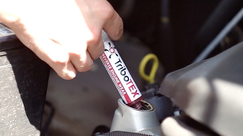 Person injecting TriboTEX additive into engine