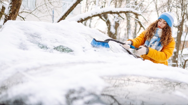 A woman scraping ice off a car's windshield