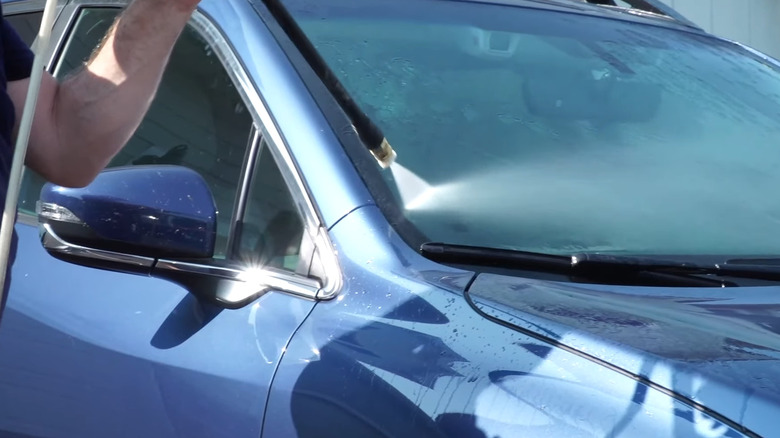 Man uses a pressure washer to clean the windshield of a car