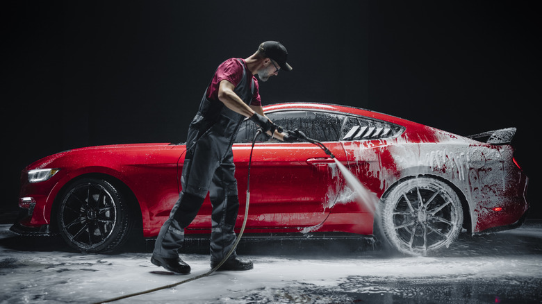 Man pressure washes a red car