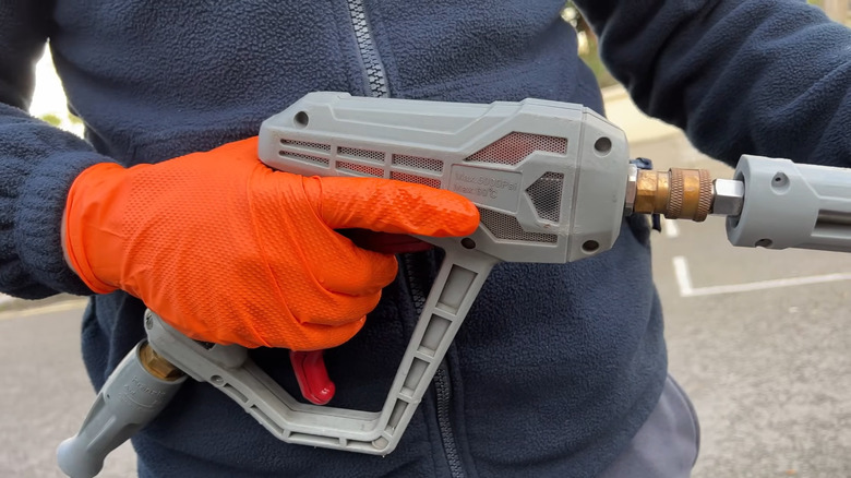 Hand holds a pressure washer with protective gloves on