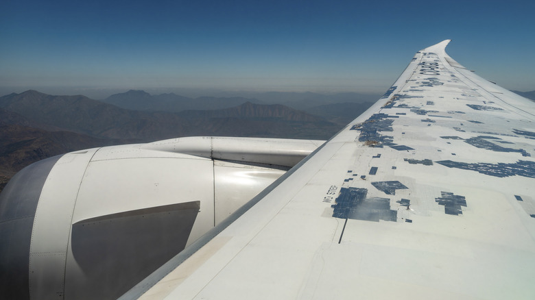 A Boeing 787 soars over a mountain scape, its wings covered in speed tape