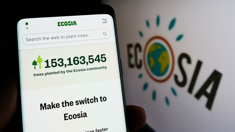 Ecosia on a smartphone with its logo on a poster in the background