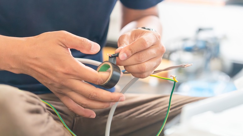 An electrician applying black electric tape on a connection.