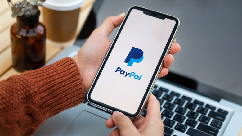 A person holding a phone displaying the PayPal logo