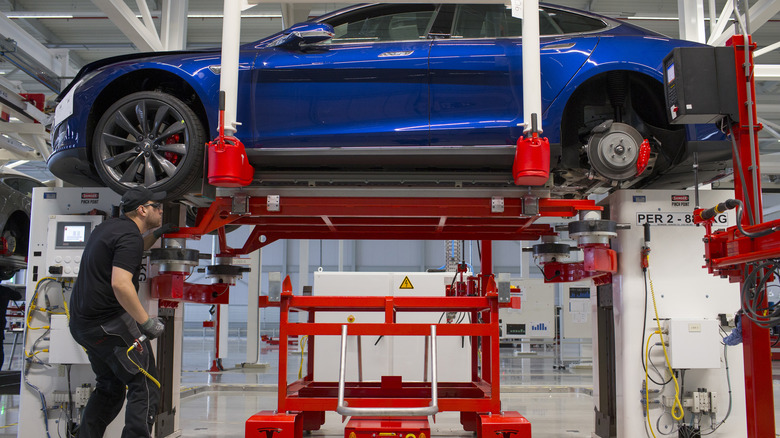 An employee fits a battery pack under a Tesla Model S automobile on the final assembly at the Tesla Motors Inc. factory in Tilburg, Netherlands