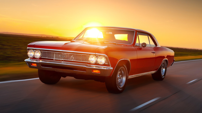 A red 1960s Chevy Malibu driving on a highway