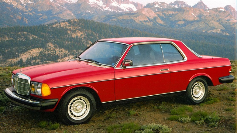 A red Mercedes-Benz 300CD parked in front of mountains