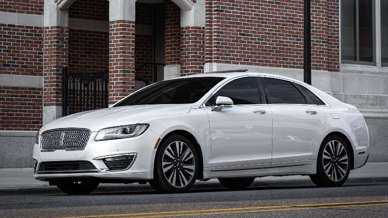 White Lincoln MKZ sedan parked in front of a red brick building